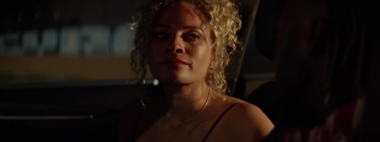 A woman with curly hair cries in a car with a man