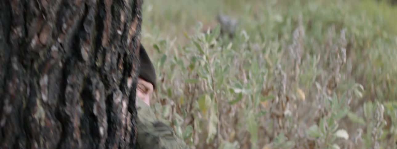 A man hides behind a tree carrying a handgun