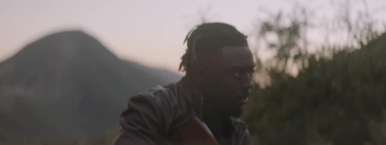 Man carrying a gun walks past hills