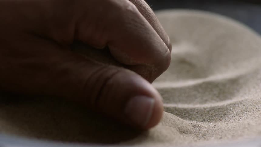 A hand scoops up sand and it sifts through the fingers