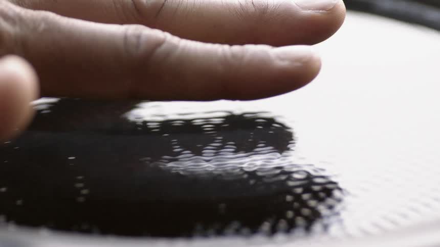 A hand hovers just above vibrating liquid in a container