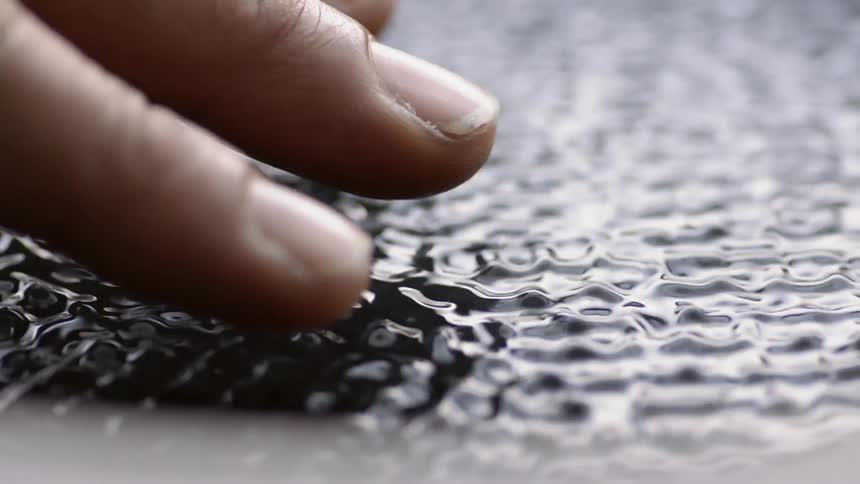 Someones finger tips are hovering above a vibrating black liquid