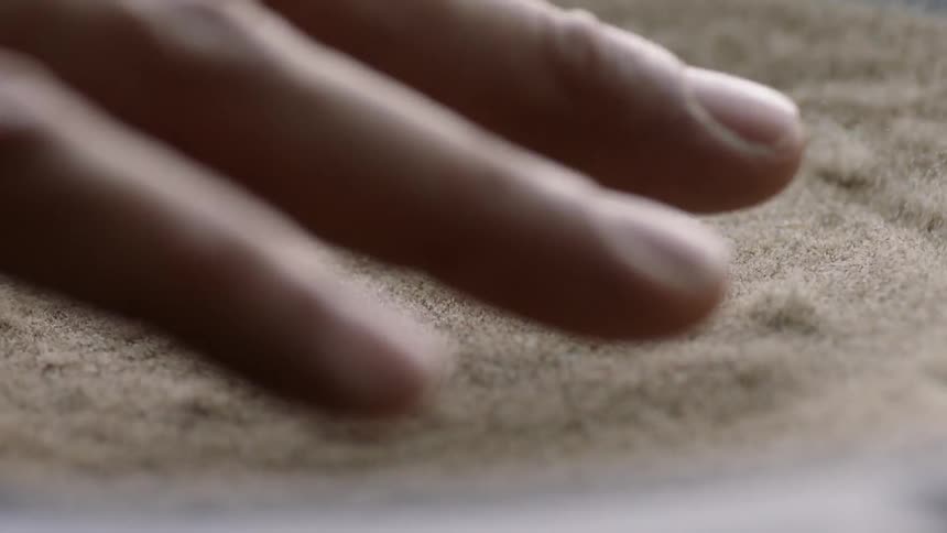 Fingers hover over vibrating sand