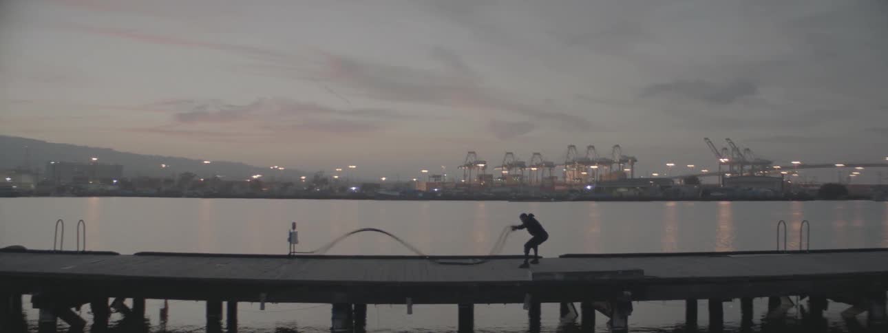 A man works out with heavy rope on a pier at sunset