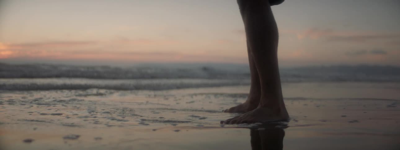 Someone is standing barefoot on the beach as the water goes over their toes
