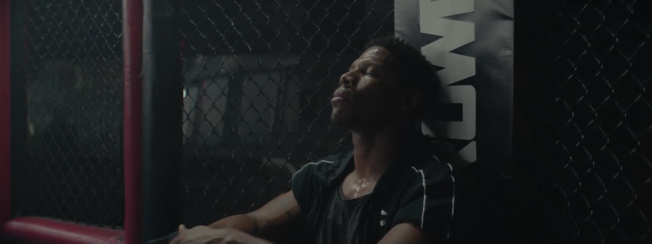 An athlete is sitting against the wall of a boxing cage