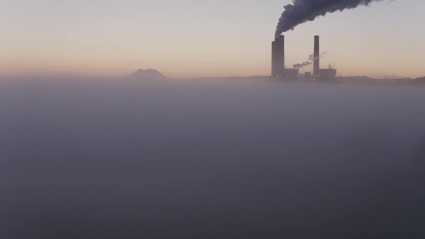 Smoke billows out from power plant smokestacks surrounded by low hanging fog