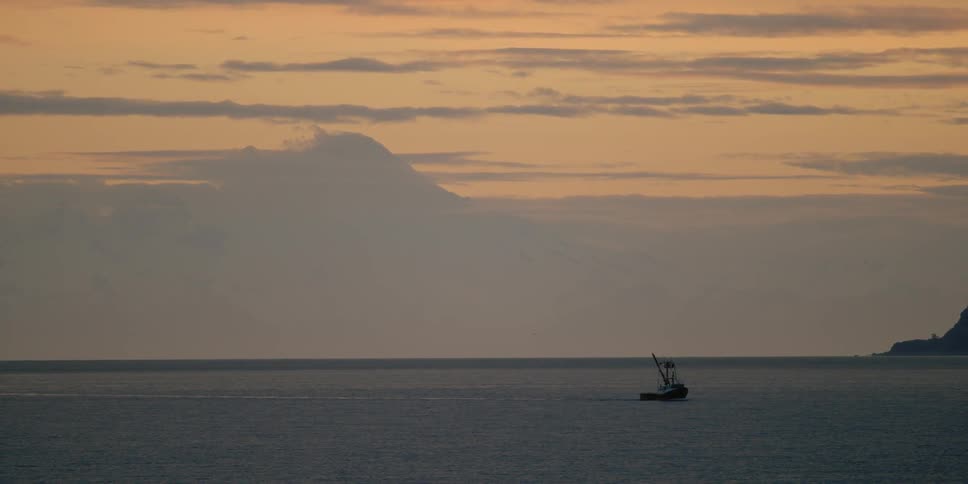 A small fishing boat in the middle of the large ocean at sunset