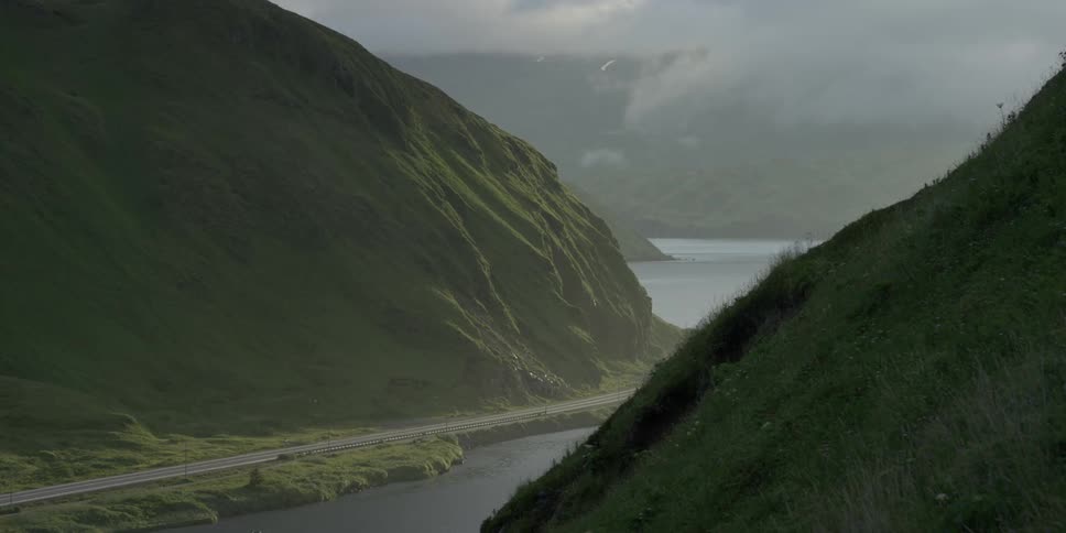 Storm clouds drift across cliffs and mountains near a coastal road during the day
