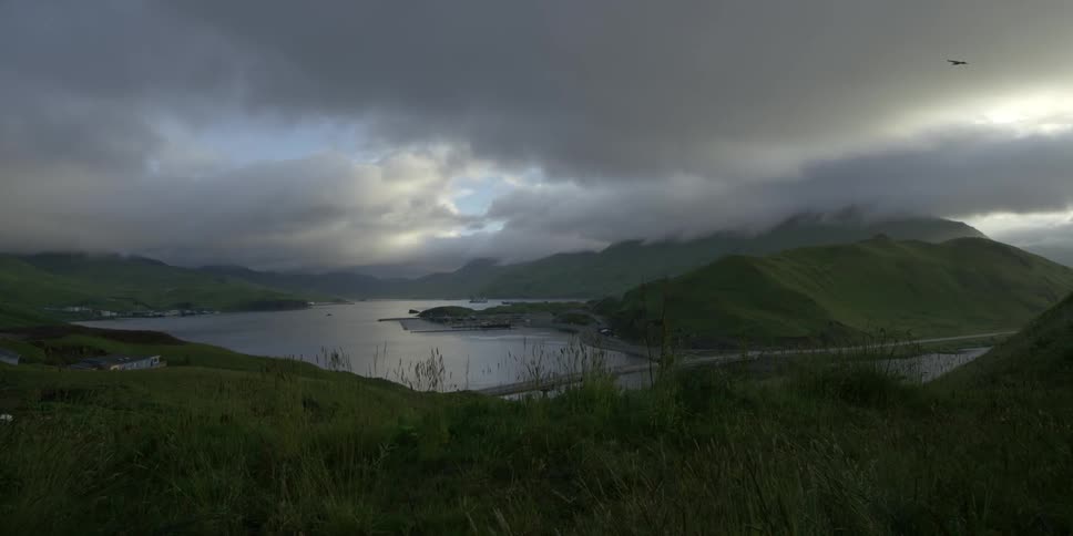A green covered hill overlooks a bay on a cloudy day
