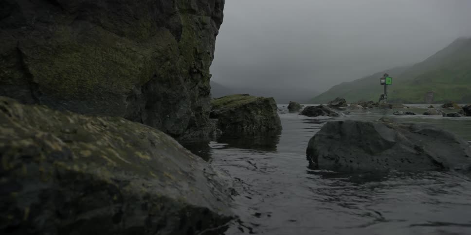 Water rippling between large rocks in foggy ocean