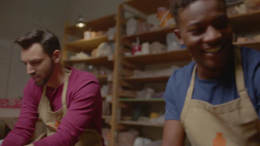 People in a pottery class smile as they work on a pottery wheel