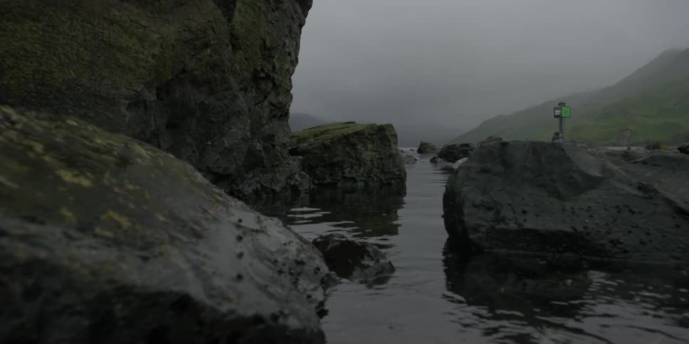 Water rippling between large rocks in ocean on foggy day