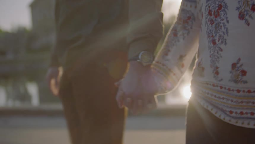 Two people hold hands and walk by the water