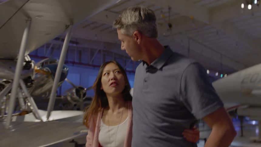 A man and woman hold on to each other as they tour an aerospace museum