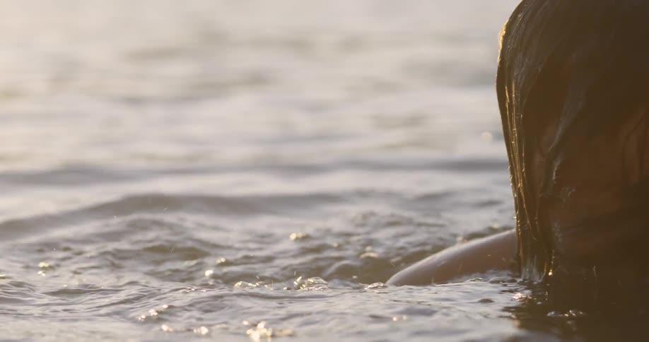 A man shakes his head and pushes back his hair as he surfaces from the water