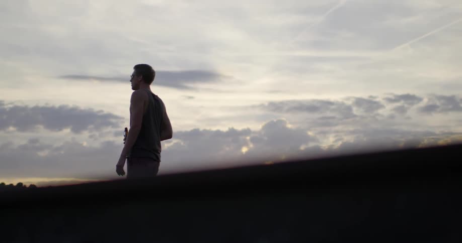 Man drinks beer while standing outside at sunset