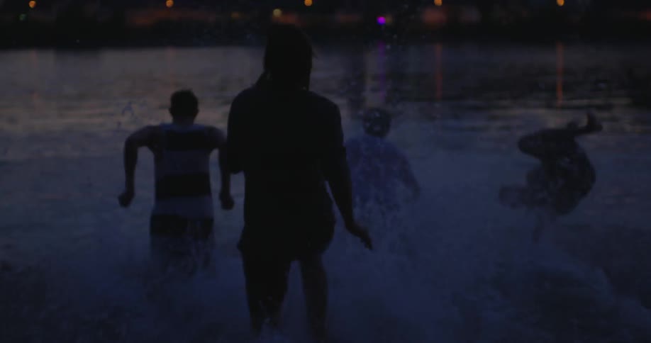 A man tosses his hat off as he and friends run into the water