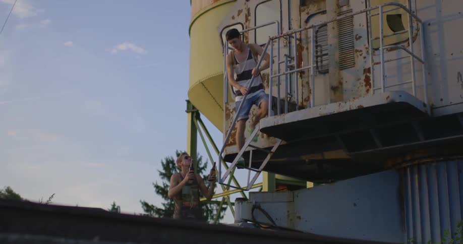 Two young men drink bottled beer outside