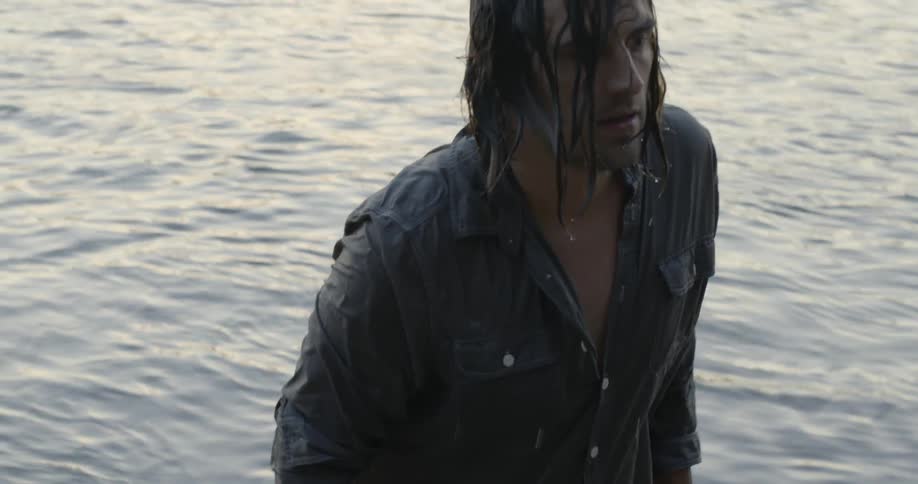 A man is walking out of a lake with his clothes dripping wet
