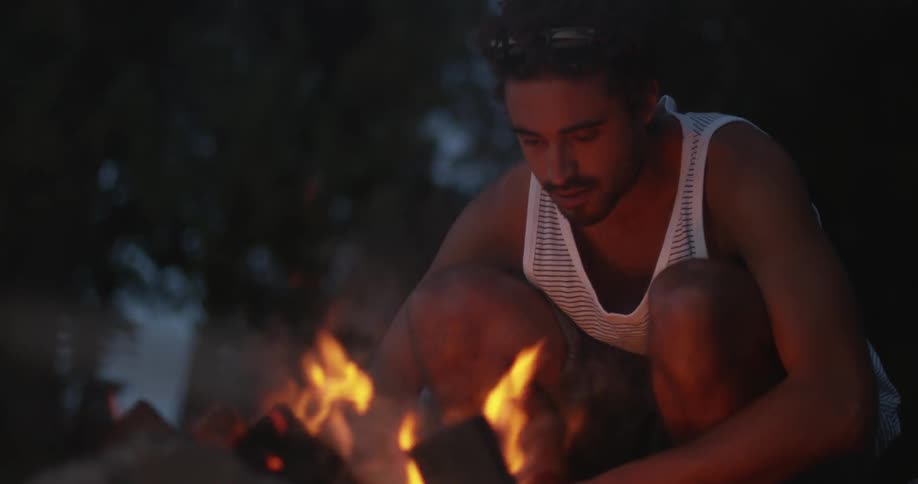 Man sits next to a campfire at night