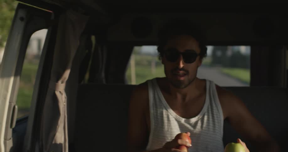 A man jumps into a moving van with apples in his hands