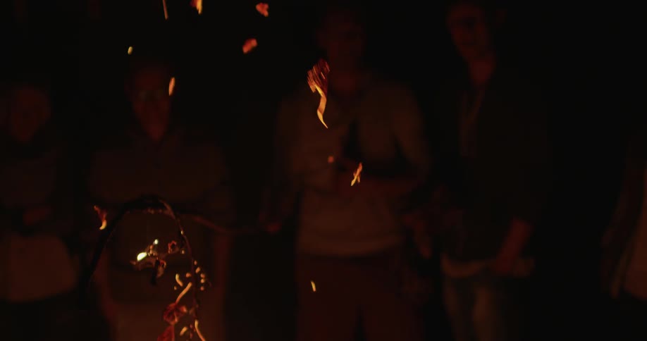 People watch as burnt leaves in a fire float up into the air at night