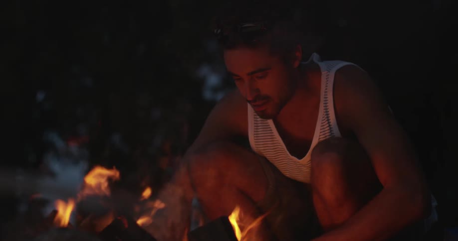 Man sits next to a campfire at night