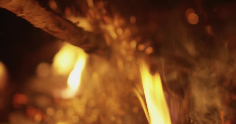 A stick is being used to stoke a campfire at night