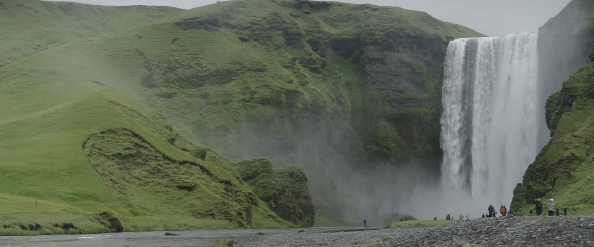 Mist flies into the sky by a large waterfall as people look on