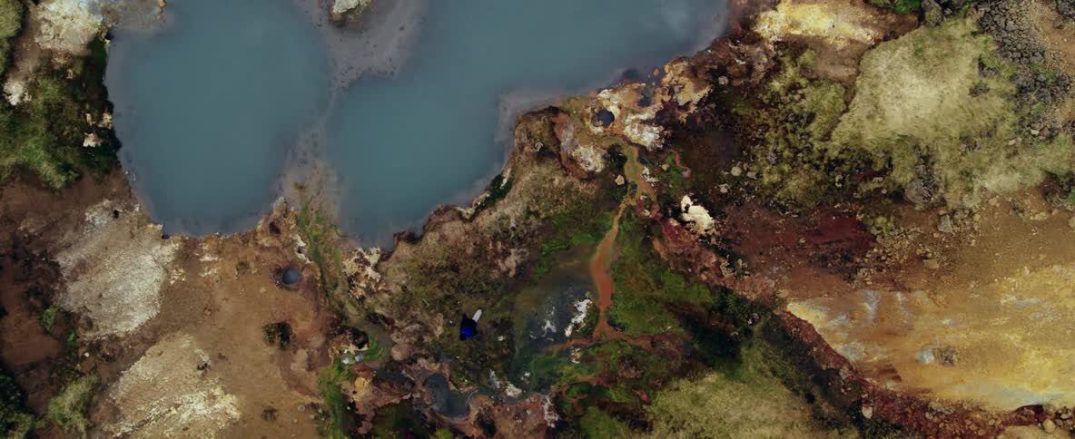 Some people are walking along the water's edge as the camera lifts straight up into the air