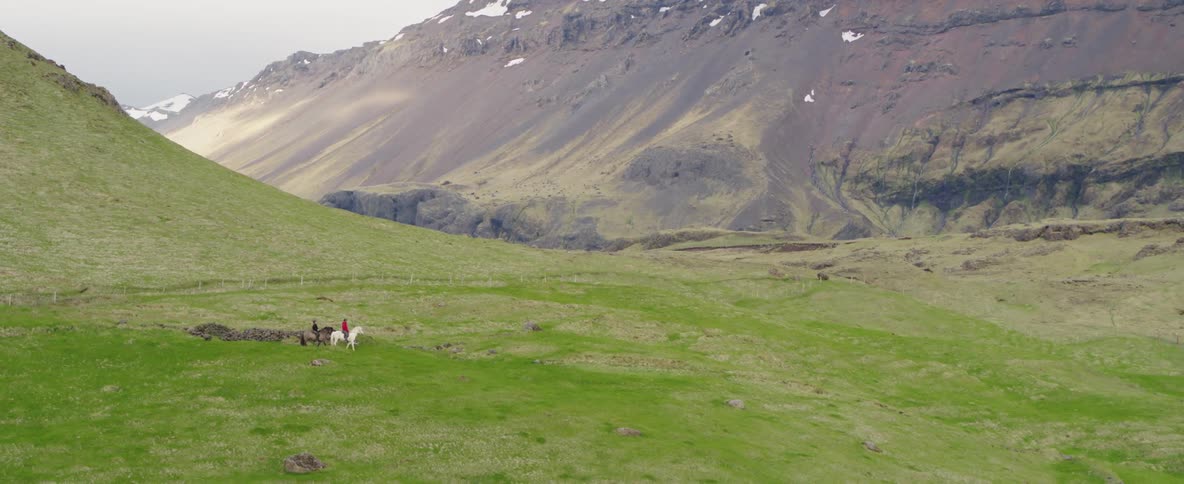 Two people on horses ride toward the mountain