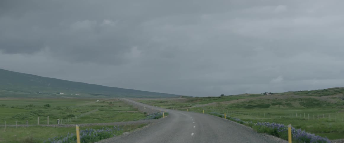 A rural road with white lines down the center leads toward the mountain
