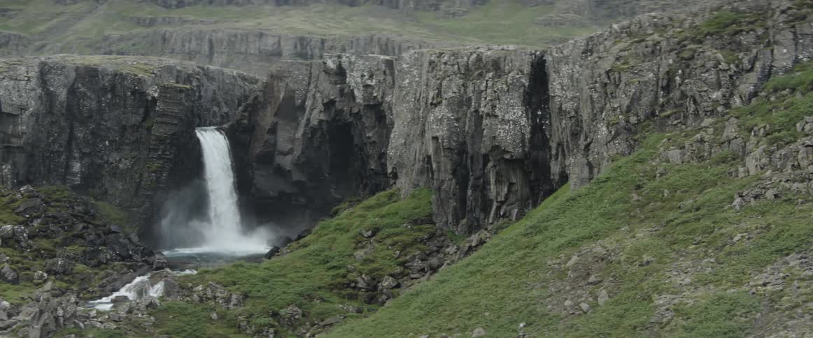 A waterfall is cascading into a pool at the base of cliffs during the day