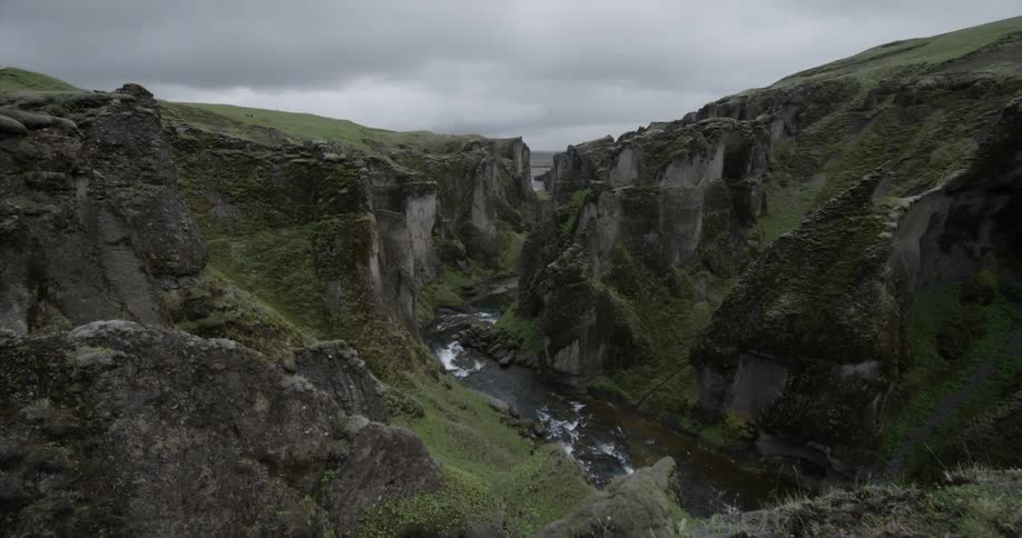 A river is running through a ravine under cloudy skies
