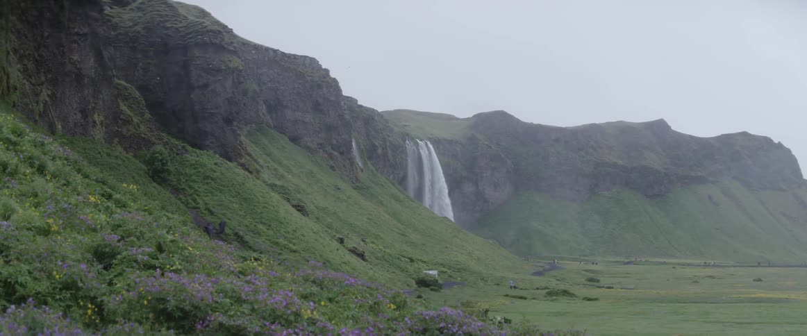 A waterfall flows over a rocky cliff on a misty day