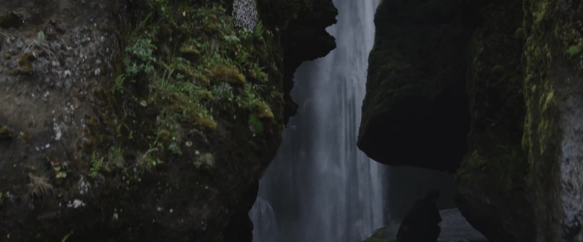 Very tall waterfall in a cavernous area with some hikers near it