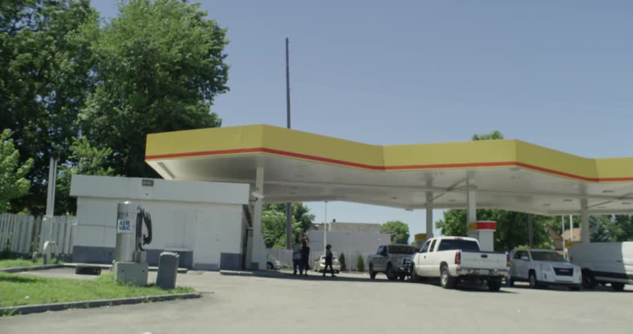 A woman is walking past a gas station during the day