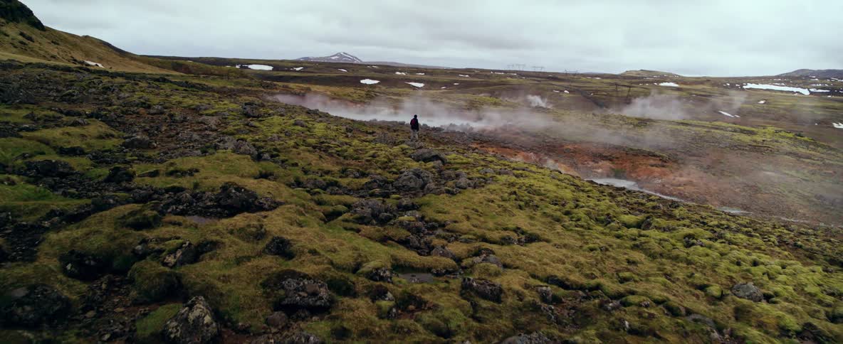 Hiker stands in a rocky field next to a steaming body of water