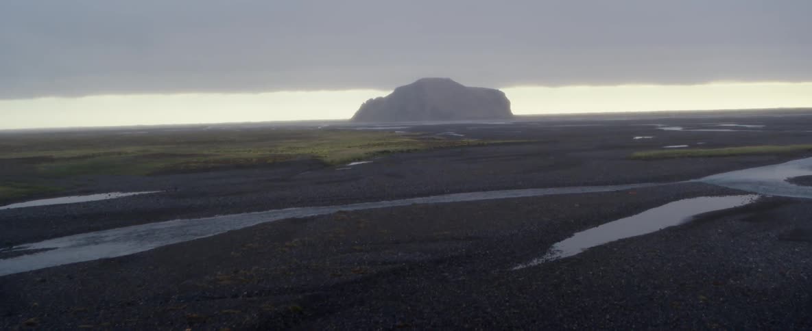 Water flows around dark sand under storm clouds