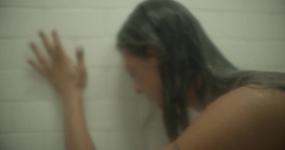 A woman is sitting in a shower crying and hitting the shower wall