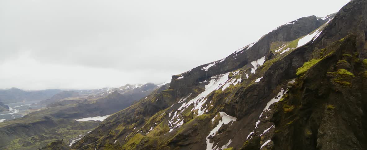 Clouds hover over a snowy mountain range during the day