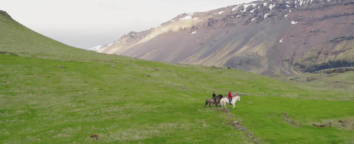 Two people ride horses through the field in the mountains