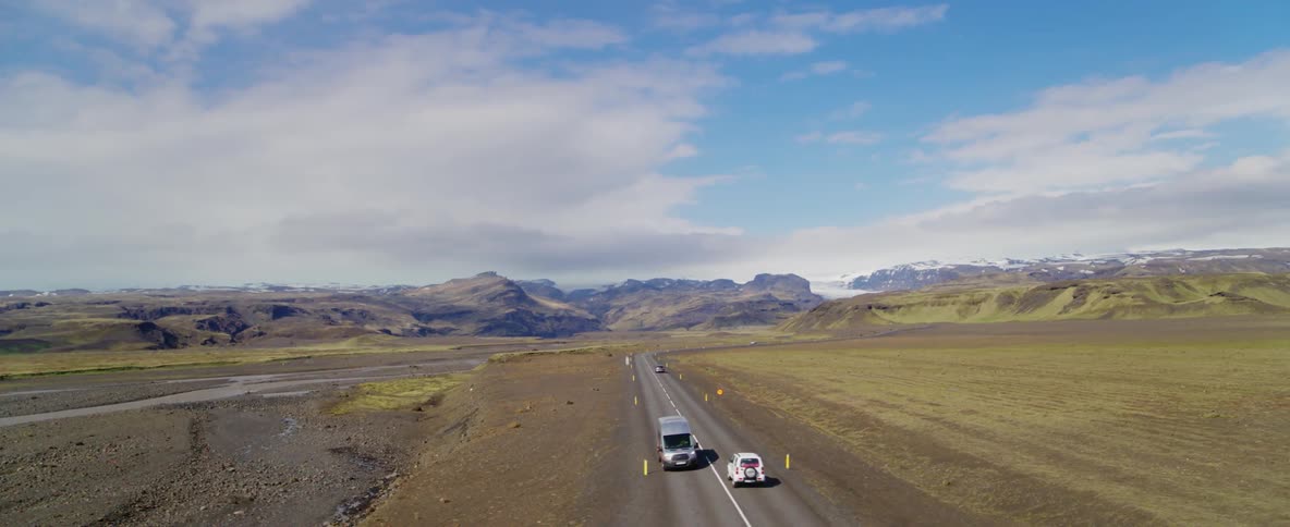 Vehicles travel down a narrow road near mountains