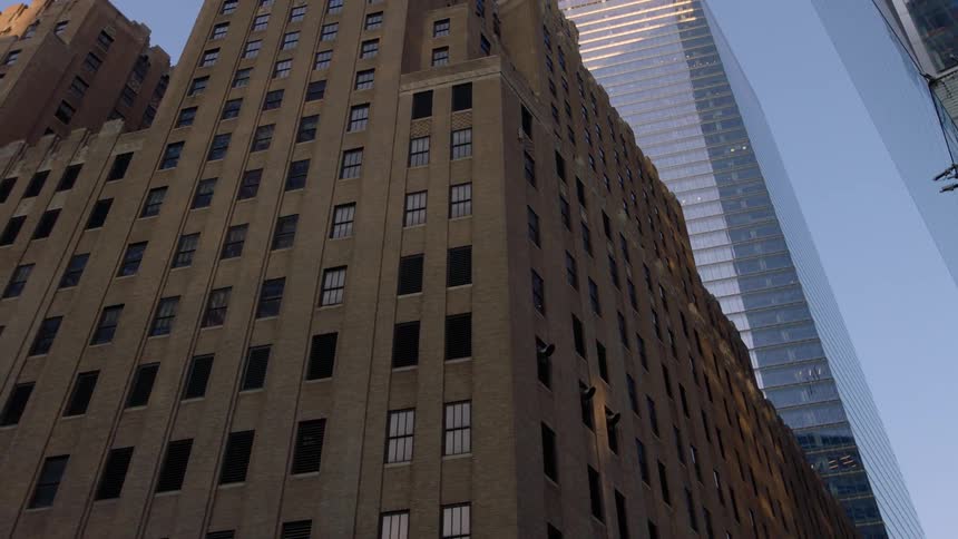 Tall city buildings tower into the sky as the sun shines