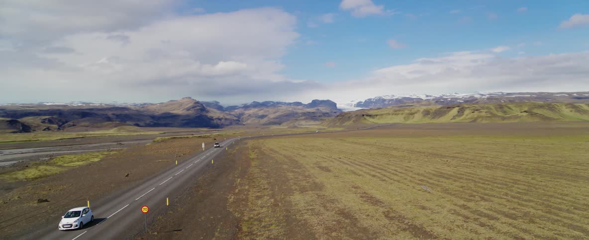 Vehicles drive on a two lane road in a mountain landscape during the day