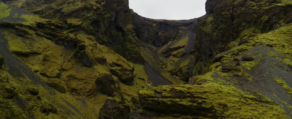 A person stands at the edge of a cliff overlooking a stream