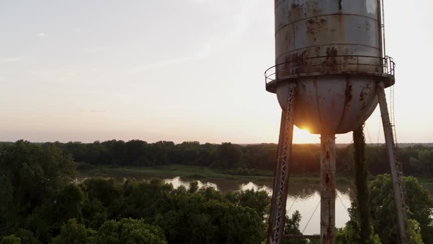 Old water tank stands by a calm river at sunset
