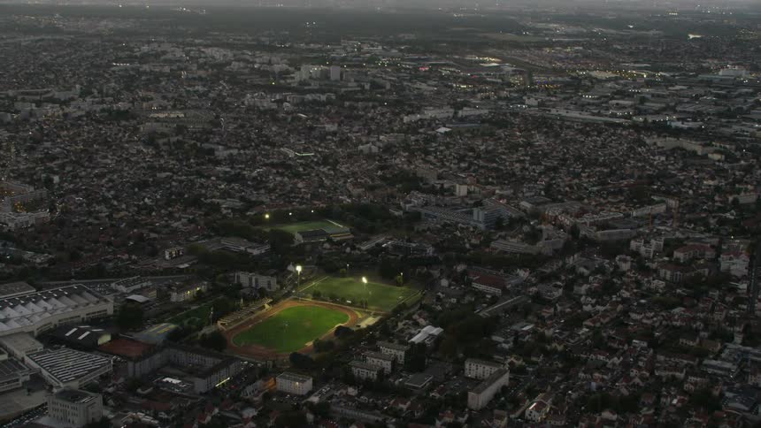 A sports park is illuminated in the middle of the city at dusk