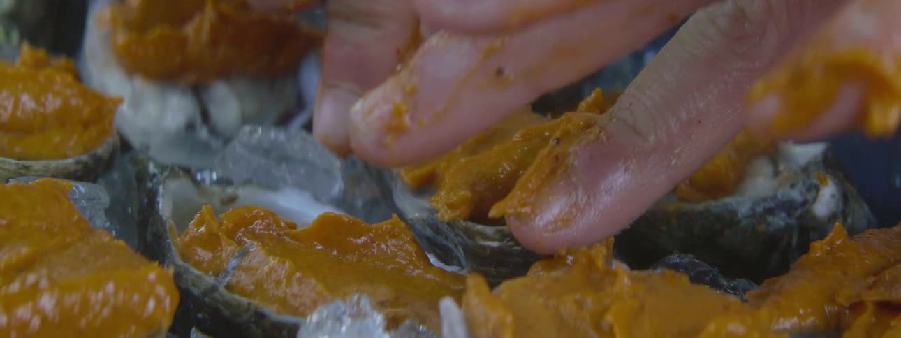 A person is spreading a mixture onto oysters during the day